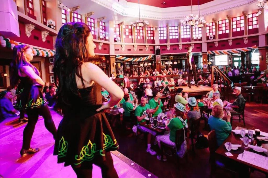 Raglan Road in Disney Springs Two irish dancers on stage with round tables on the floor full of people dressed in green and Irish attire.