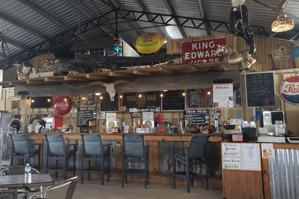 Showcase of Citrus Typical Floridian bar with an old table and many bar stools along. They are different signs of various colours, one says King Edward on it. There is also an alligator on a platform above the bar.