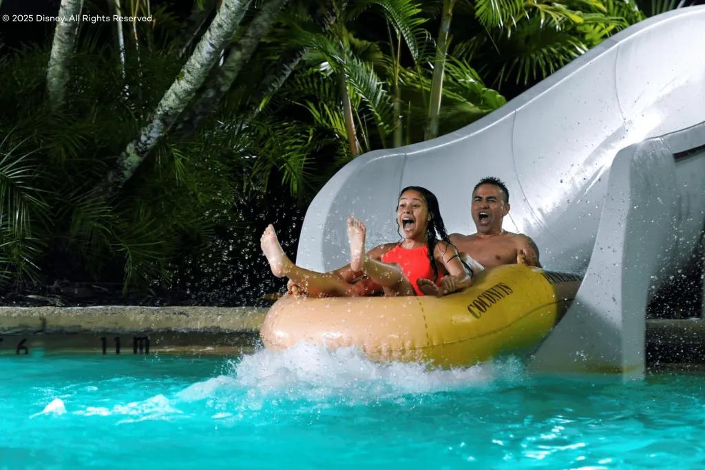Disney H2O Glow After Hours A woman and man plummeting down a white water slide into the pool below sat in a yellow double rubber ring.