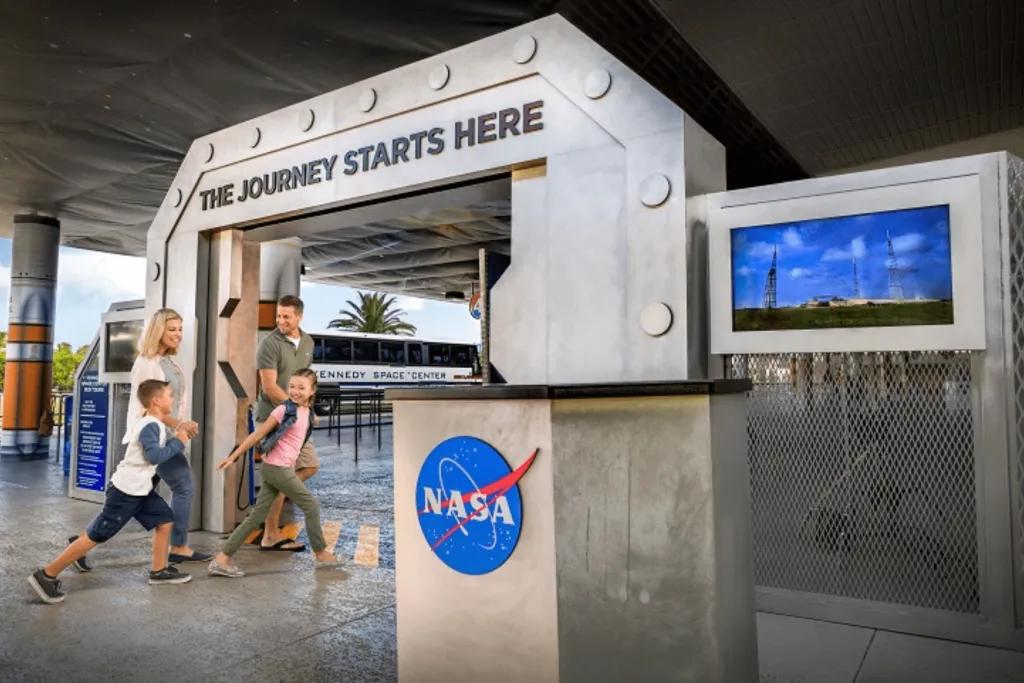 Kennedy Space Center Family walking under banner which says "Your journey starts here" with a bus waiting for them.