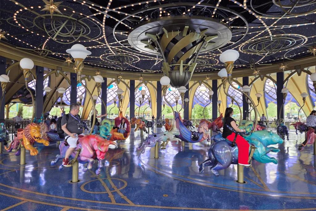 Constellation Carousel People riding a carousel inside of a beautiful purple ride with star constellations on the ceiling. There are different creatures you can choose to go on, each hand carved.