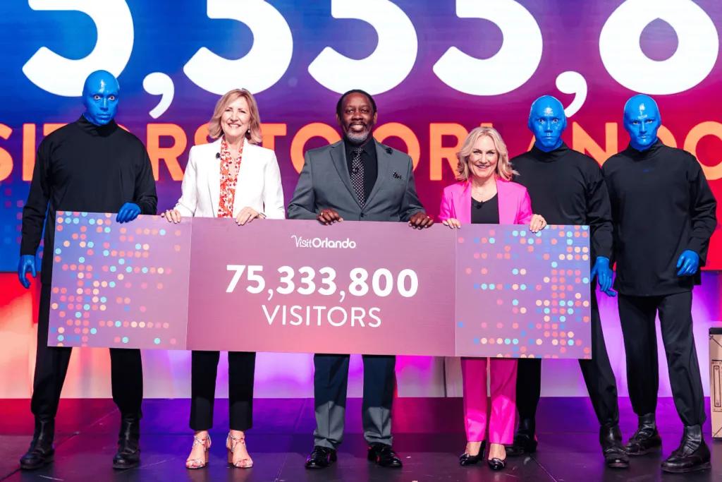 Orlando Visitors Three professionals at conference holding up a sign that announces Orlando had 75,333,800 visitors