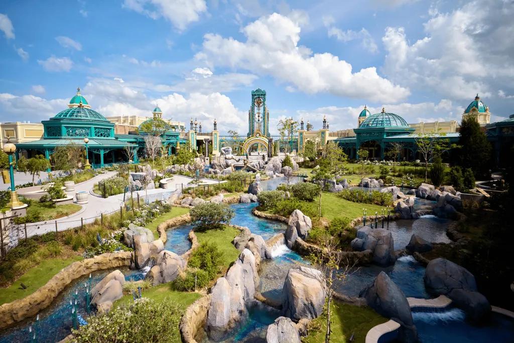 Celestial Park Large garden space with rocks, greenery and small ponds of water. In the background you can see buildings including the Constellation Carousel, as well as the Epic portal.