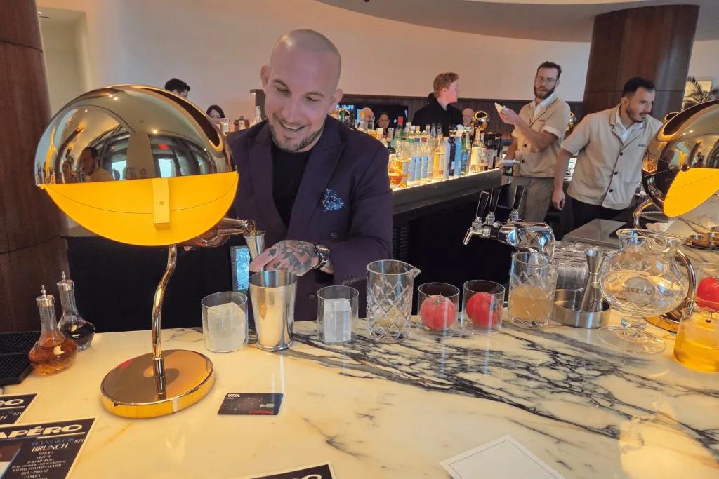Apero Bar Bartender pouring drinks behind a bar with gold decorations including a large lamp.