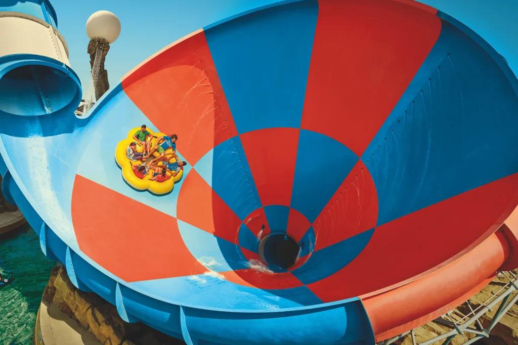 Dawwama A group of people in a yellow rubber ring dropping down large drop into a funnel water slide.