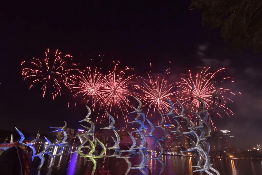 Fireworks at the Fountain Lake with multiple different fireworks bursting in the sky, one spiralling multi-coloured.
