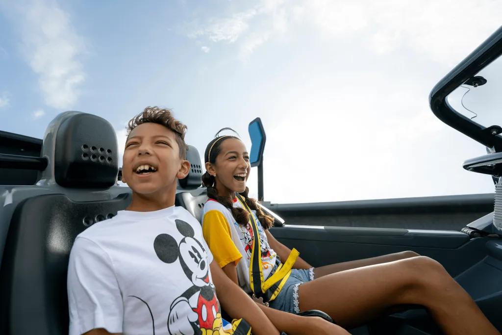 Test Track Boy and girl sat on a car shaped rollercoaster vehicle smiling and laughing with joy as they travel at high speeds around a corner.