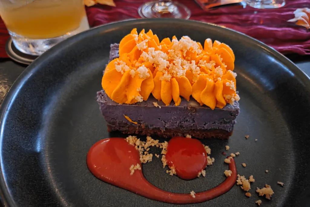 Raglan Road Purple cheesecake with orange icing and a red sauce with some biscuit crumbs on top.