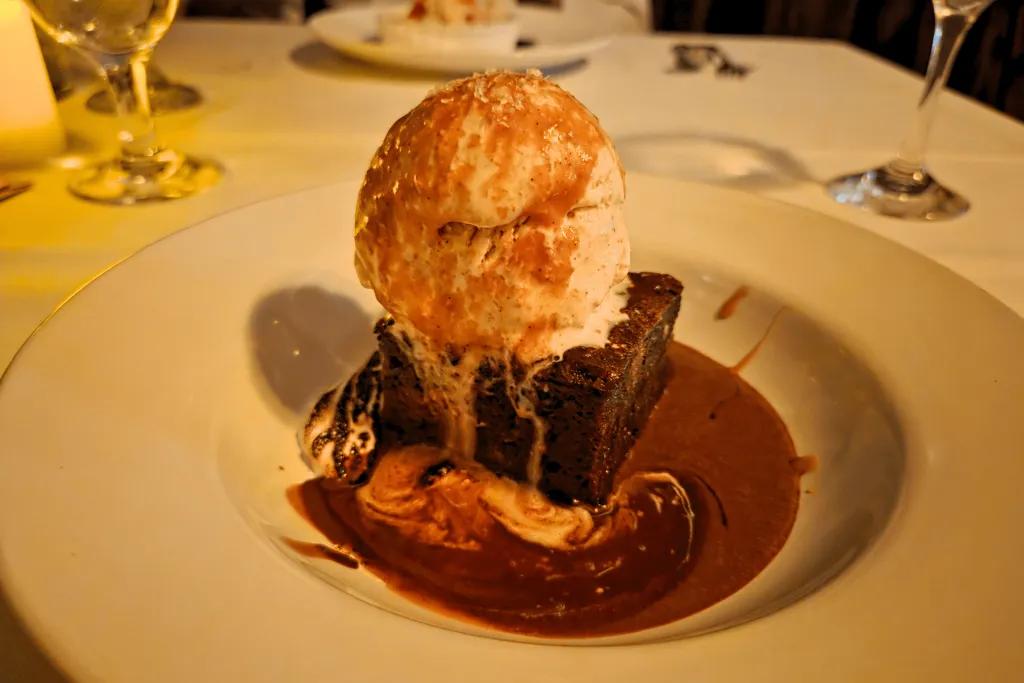 Brownie dessert Large square brownie in a chocolate sauce with a large scoop of ice cream on top and caramel drizzled over.