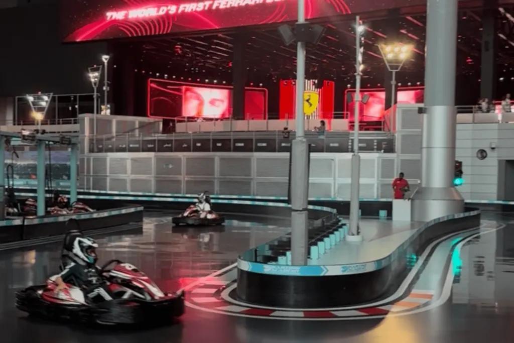 Karting Academy Go karts racing around an indoor track with a large Ferrari sign in the background.