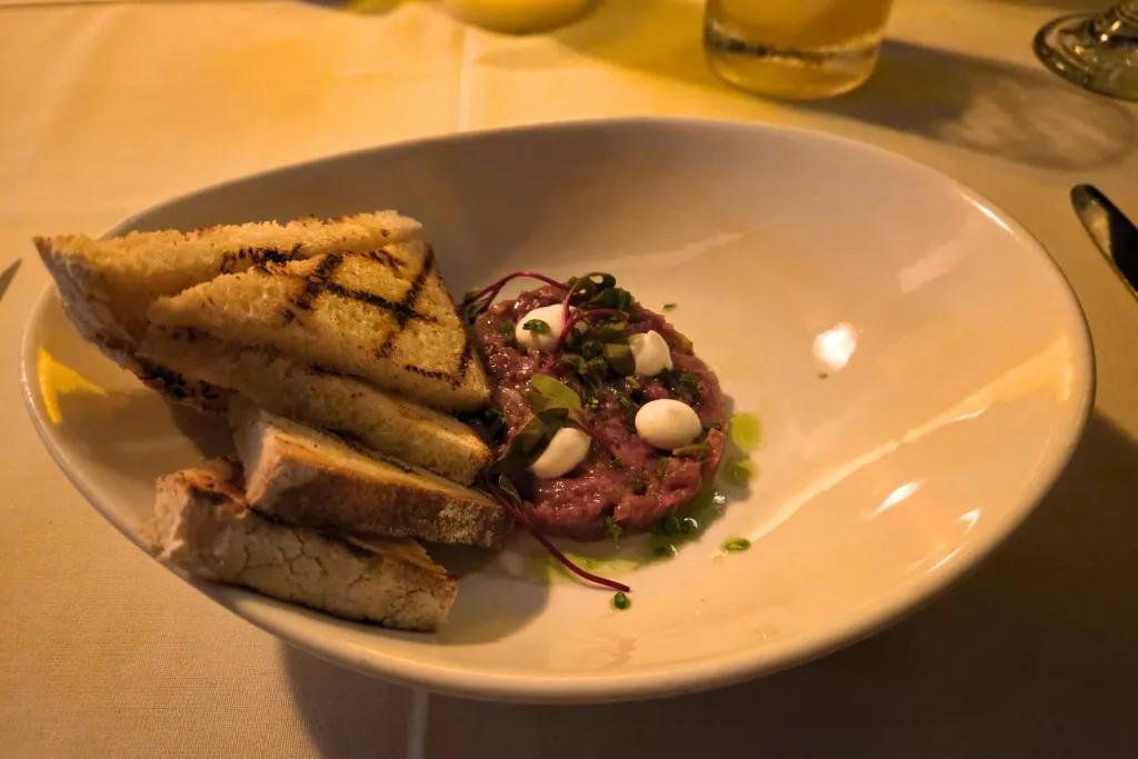 Beef Tartar Starter Circular slice of beef with white sauce on top and triangular slices of bread on the side