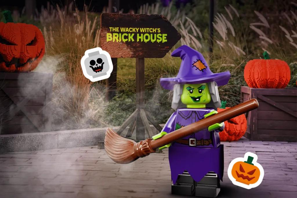 LEGOLAND Dubai Halloween Green witch lego character stood with broom stick by a sign saying - The Wacky Witch’s Brick House. There are also lego pumpkins behind.