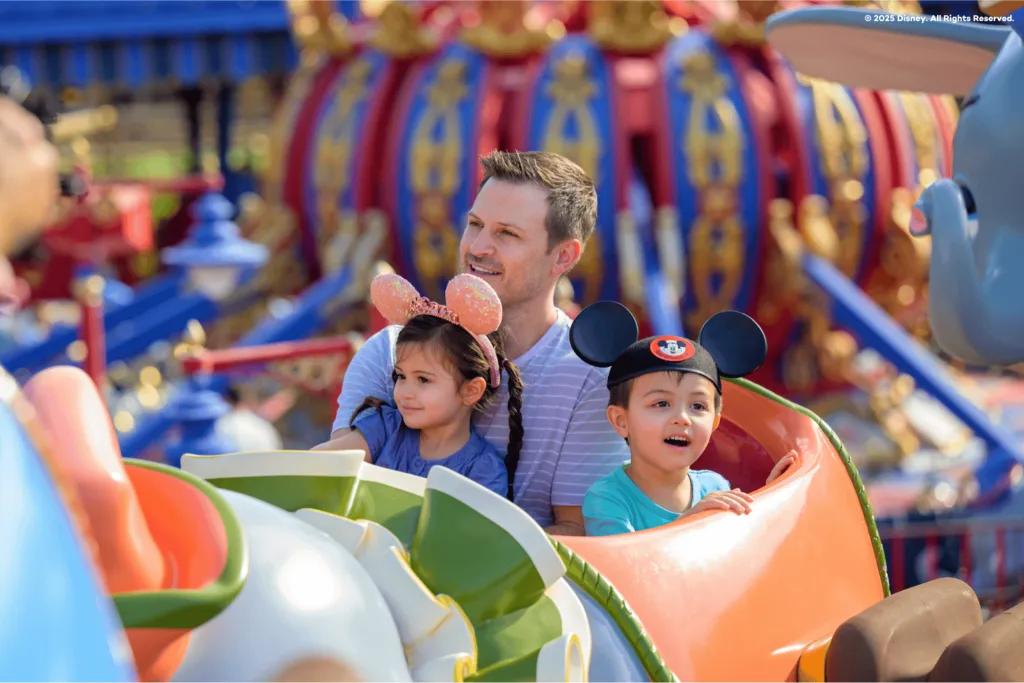 A father riding the classic Dumbo the Flying Elephant attraction in Magic Kingdom with his two smiling young children, showcasing a perfect family ride at Walt Disney World Resort.