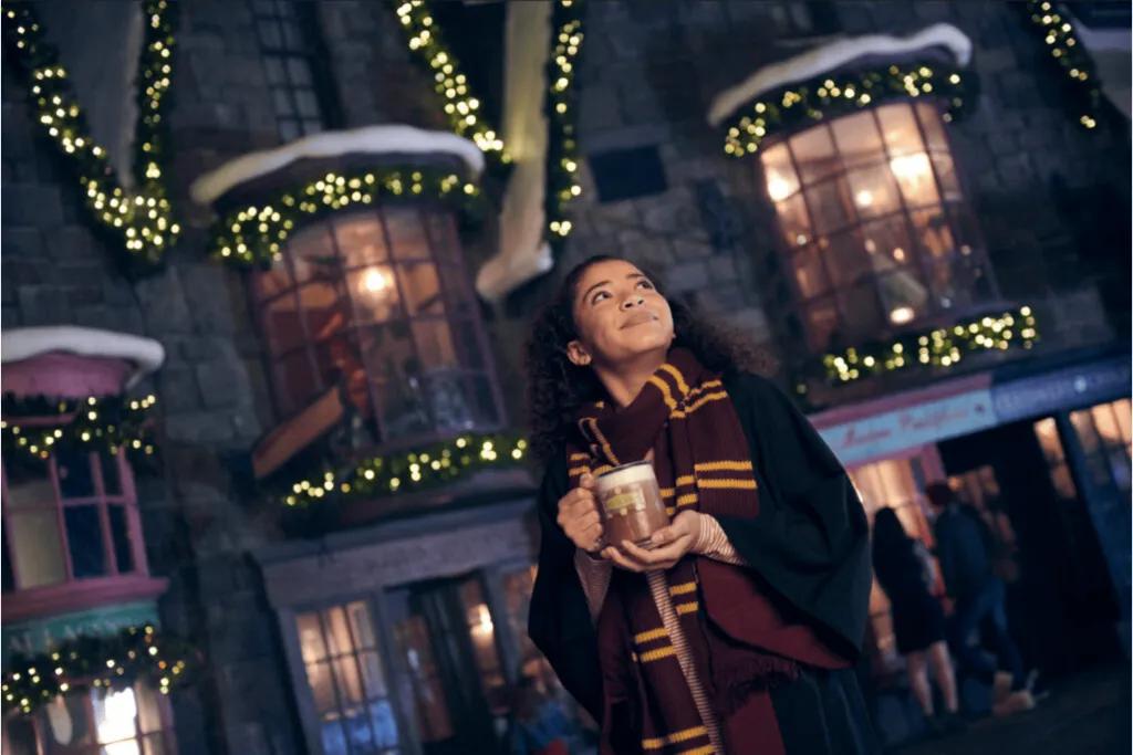 A young guest smiles while enjoying Butterbeer in the festively decorated and covered streets of The Wizarding World of Harry Potter at Universal Studios Florida - a great place to stay dry when it's raining at the resort.