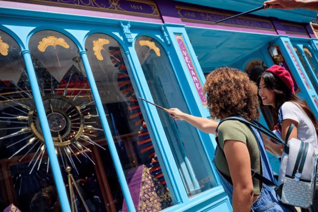 Guests using their Harry Potter wands to trigger a magical effect in a shop window display, showcasing a popular and immersive souvenir experience at Universal Orlando Resort.
