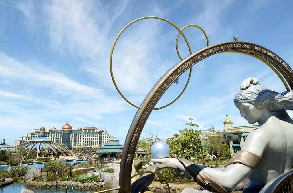 Grand hotel in background, Constellation Carousel and a statue of a goddess standing above a theme park.