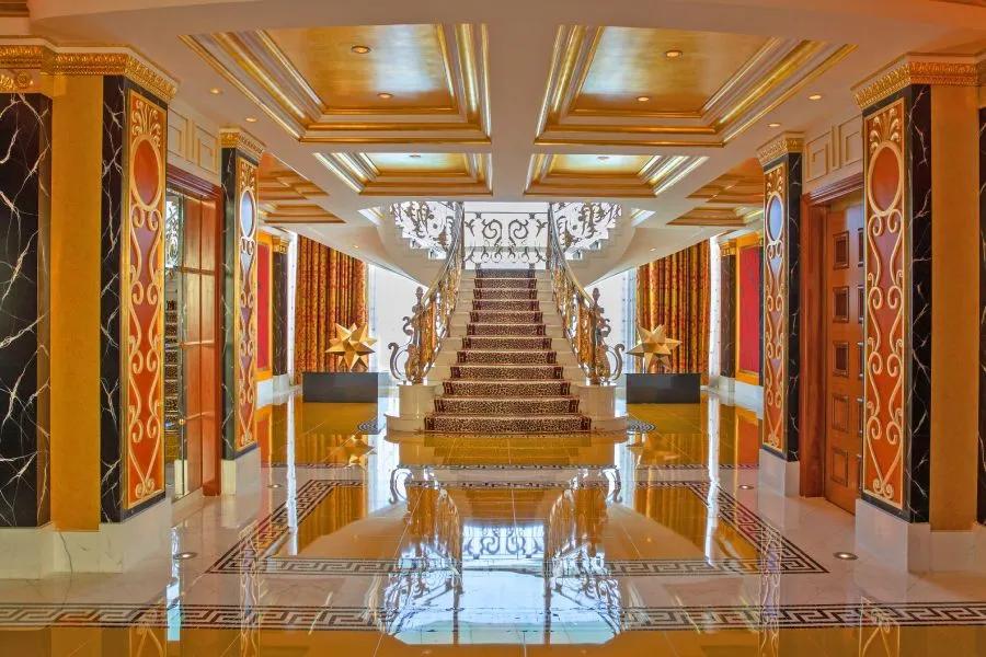 Burj Al Arab's spectacular interior lobby with high gold ceilings, reflective marble floors, and a sweeping grand staircase.