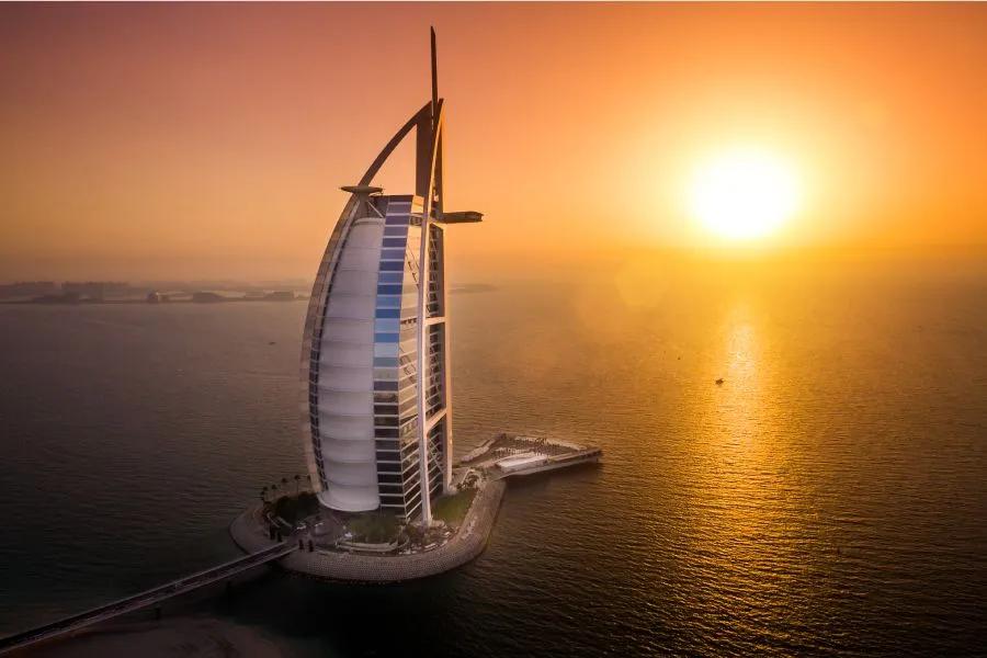 Sail-shaped Burj Al Arab hotel in Dubai set against a dramatic orange sunset over the Arabian Sea.