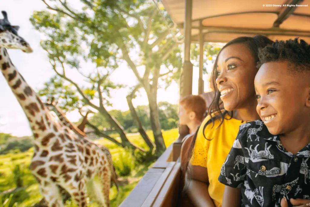 A woman and child smiling while watching a giraffe from a safari vehicle at Disney’s Animal Kingdom