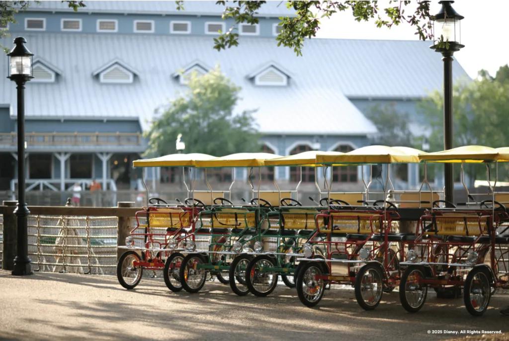 A row of colorful four-wheel Surrey bikes with yellow fringed tops parked at a Disney resort