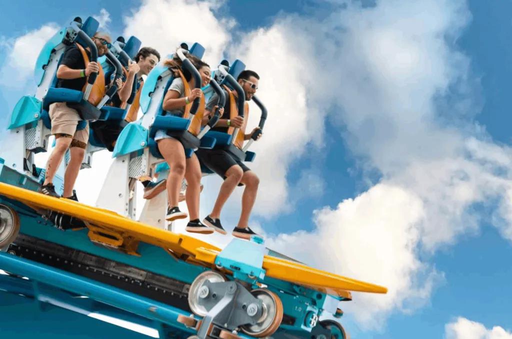 A group of riders standing on the SeaWorld Pipeline: The Surf Coaster as it glides along a blue track against a bright, cloudy sky.