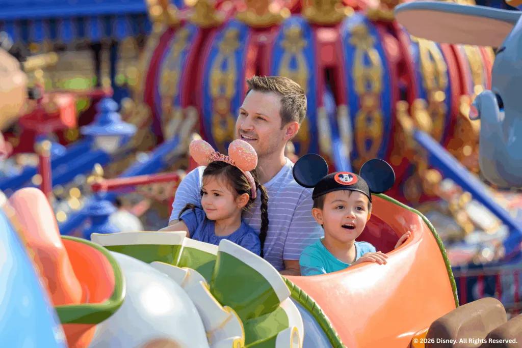 Father and two children wearing Mickey ears riding Dumbo the Flying Elephant