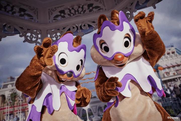 Chip and Dale in purple and white Halloween costumes waving at the Disney Halloween Festival