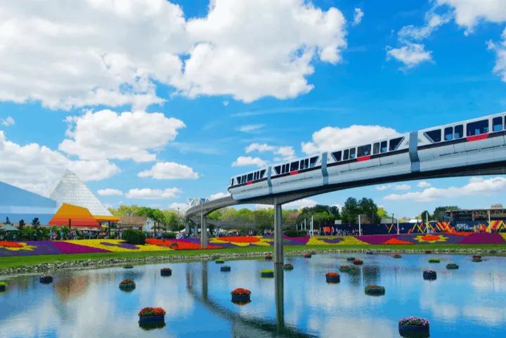 Monorail passing over a lake with colorful flower gardens at EPCOT, with the Imagination Pavilion in the background