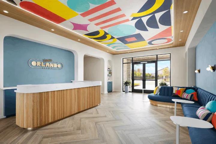 Colorful lobby with front desk and lounge seating at Villatel Orlando Resort, featuring a bold geometric ceiling mural