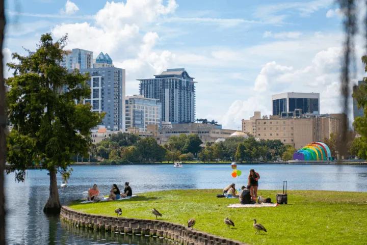 People picnicking on the grass by Lake Eola with the downtown Orlando skyline in the background