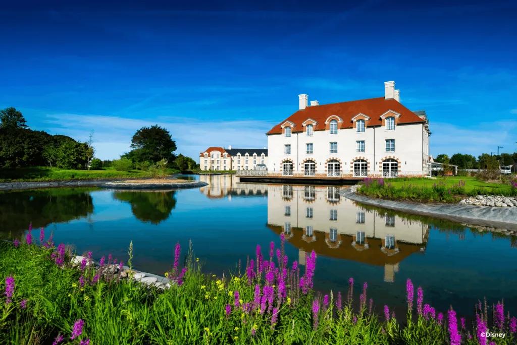 Staycity Aparthotels Paris, Marne-la-Vallée reflected in a pond bordered by purple wildflowers under a clear blue sky