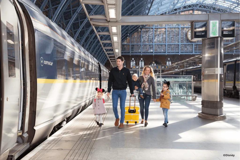 A family with young children in Disney ears walking along the platform beside a Eurostar train at St Pancras International