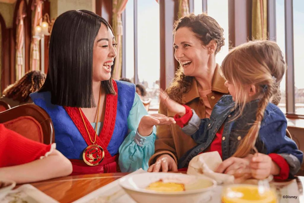 Guests laughing with Mulan at their table during breakfast at The Regal View Restaurant & Lounge, Disney Adventure World