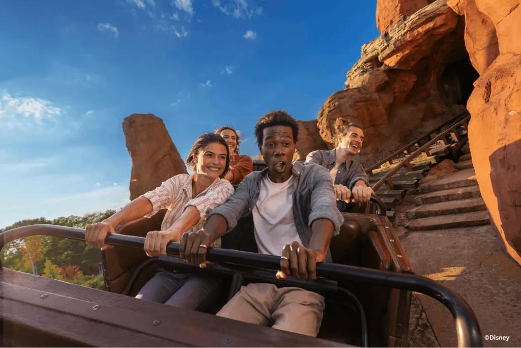 Guests riding a mine train through red rock formations on Big Thunder Mountain at Disneyland Park