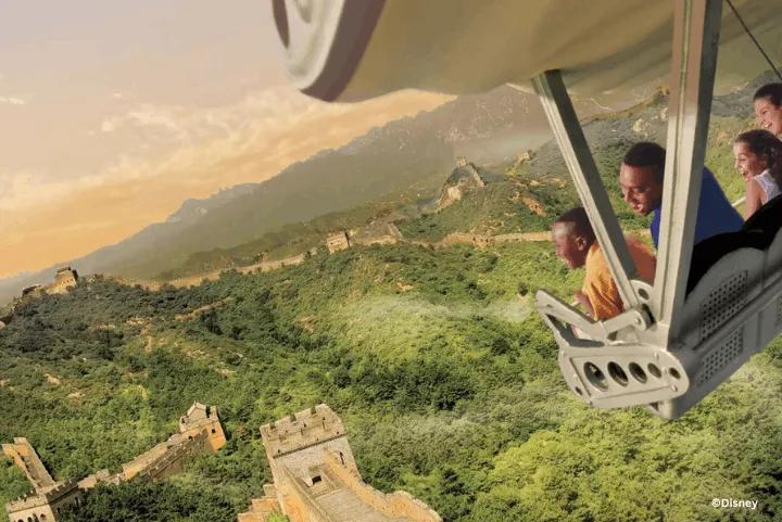 Guests seated in the hang-glider simulator vehicle on Soarin' Around the World, smiling as they fly over a projection of the Great Wall of China