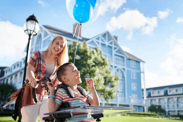 A mother pushes a boy in a wheelchair holding a blue Mickey balloon at Disney's Beach Club Resort