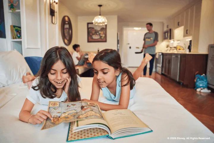 Two young girls reading a map on a bed while their family relaxes in a villa suite