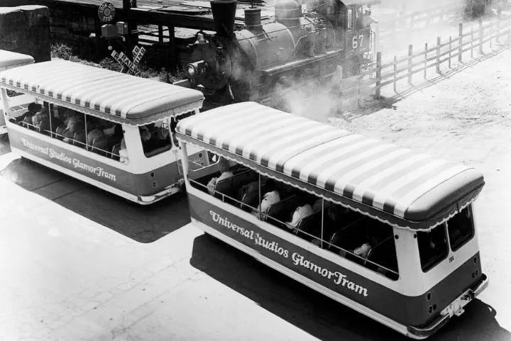 Vintage black-and-white photo of Universal Studios Glamor Tram cars passing a steam train