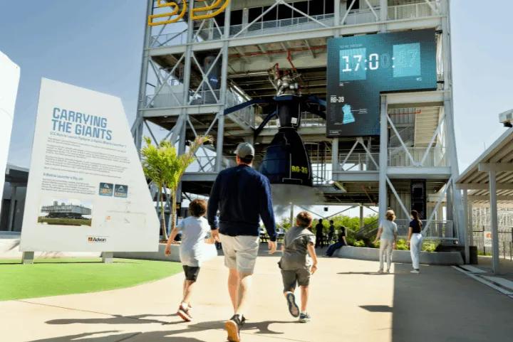 Visitors walking toward the LC-39 gantry structure with a large rocket engine exhibit