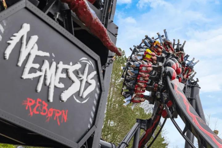 Riders banking through a turn on Nemesis Reborn beside its entrance sign at Alton Towers
