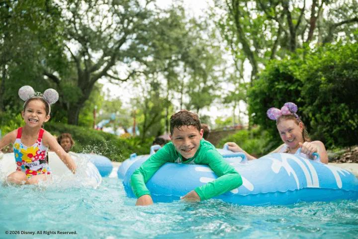 A family smiling and floating on blue inner tubes down the lush, tree-lined Cross Country Creek lazy river at Disney's Blizzard Beach Water Park