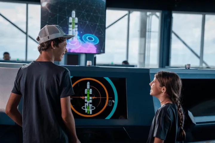 Two children using interactive consoles inside the Rocket Builder exhibit