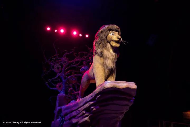 Simba standing atop Pride Rock on a stage float under red theater lights during Festival of the Lion King