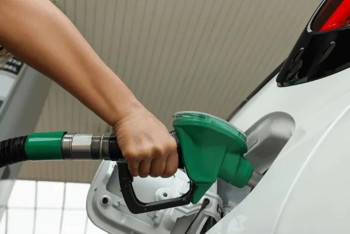 Person holding a green fuel nozzle while refueling a white car