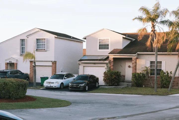 Two suburban houses with cars parked in the driveways and palm trees in the front yard