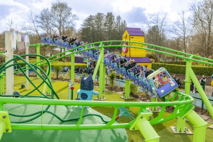 Families riding the colourful Bluey the Ride: Here Come the Grannies! coaster past a yellow themed house at Alton Towers
