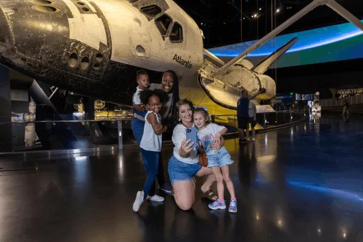 A group taking a selfie in front of the Space Shuttle Atlantis display