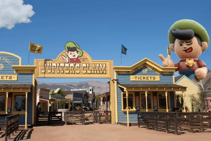 Western-themed entrance archway to Jupiter's Claim with ticket booths and a large character mascot balloon