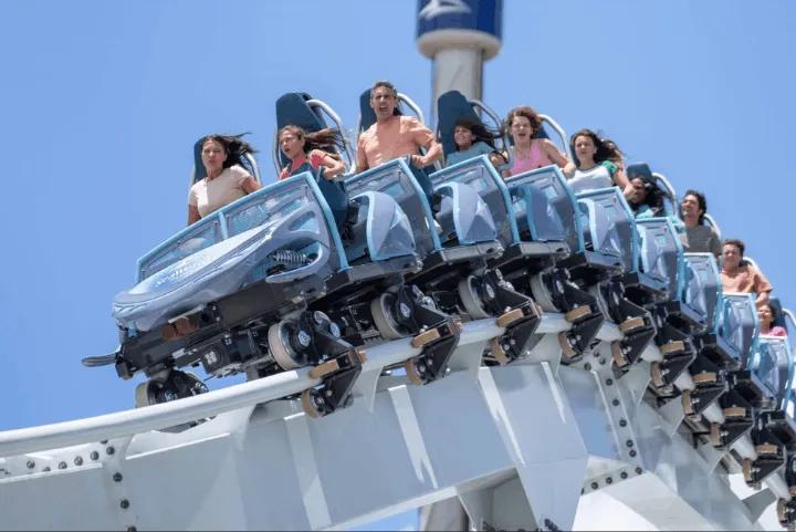 Riders cresting a hill on Penguin Trek roller coaster against a clear blue sky at SeaWorld Orlando