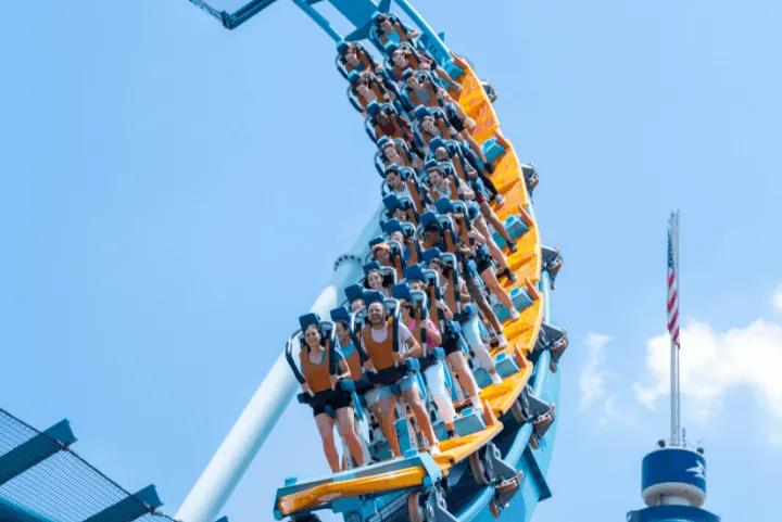 Riders on Pipeline: The Surf Coaster winding through a tight orange-track turn against a blue sky at SeaWorld Orlando